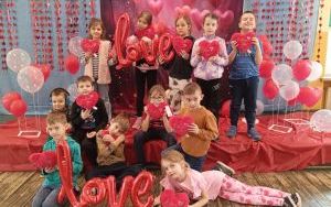 Zdjęcie grupowe klasy 1b na scenie udekorowanej balonami i serduszkami