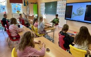 Dzieci siedzące w ławkach, słuchające prelekcji i wiersza na temat instrumentów dętych